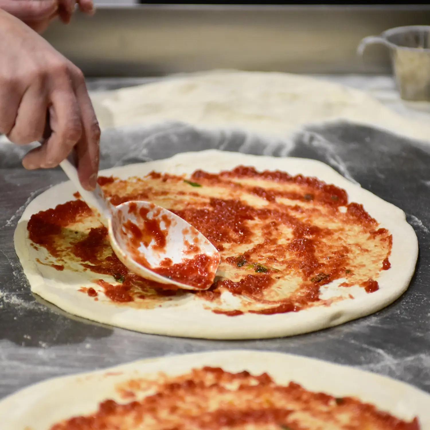 Kokki levittää tomaattikastiketta pizzan päälle