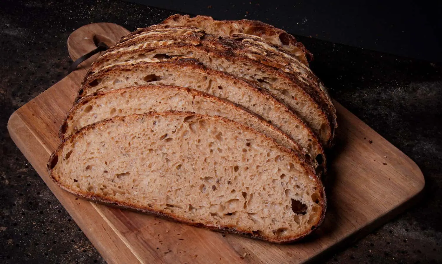 Siivutettu tumma juurileipä puisella leikkuulaudalla